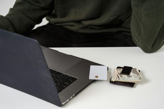 A man shopping online with a laptop, money, and a card