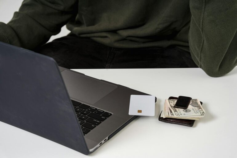 A man shopping online with a laptop, money, and a card