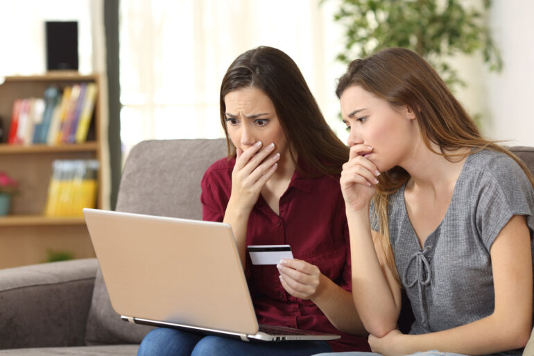 Two women looking nervously at the laptop while holding a credit card