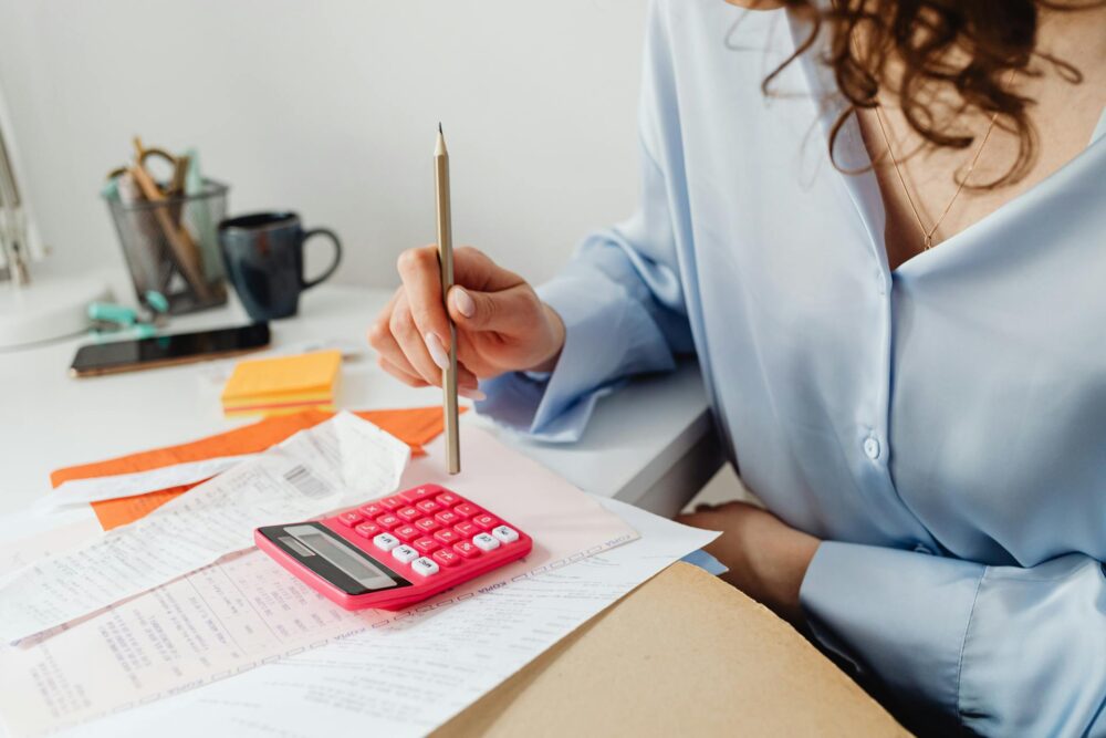 A woman reviewing merchant statements using a pink calculator